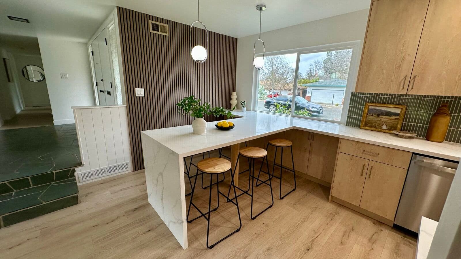 Kitchen with white-oak cabinets, waterfall quartz peninsula, wood stools, pendant lights, and a wood slat accent wall