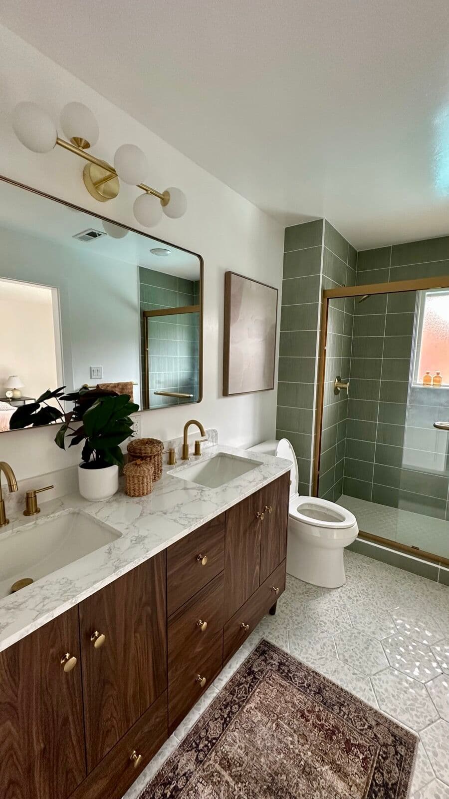 Primary bathroom with a walnut double vanity, brass fixtures and a sage tile shower