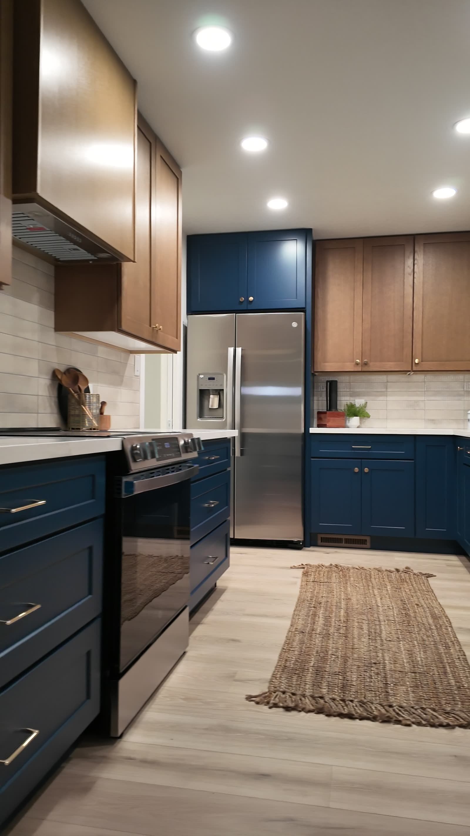 Finished kitchen with navy base cabinets, white-oak uppers, stainless range and refrigerator, and light wood-look floor