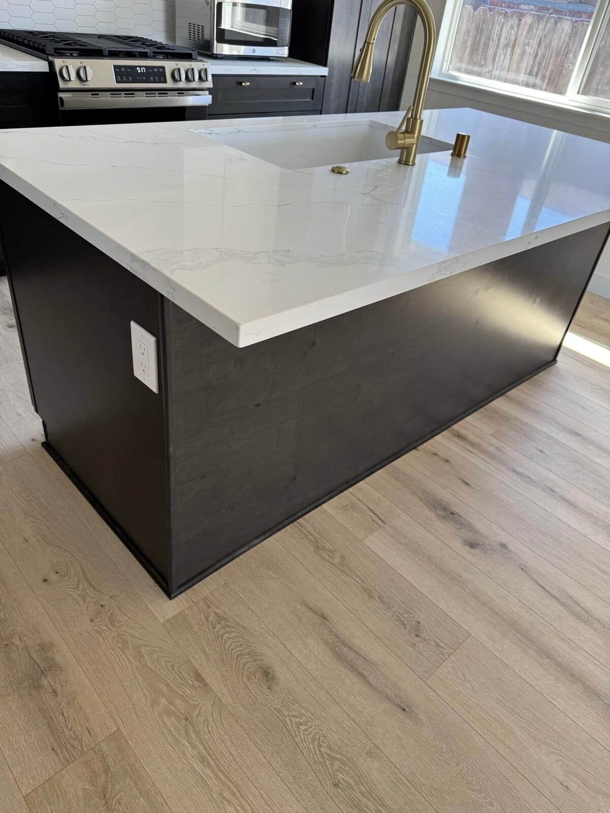 Marble-look quartz island edge with a brass faucet and dark cabinet panel