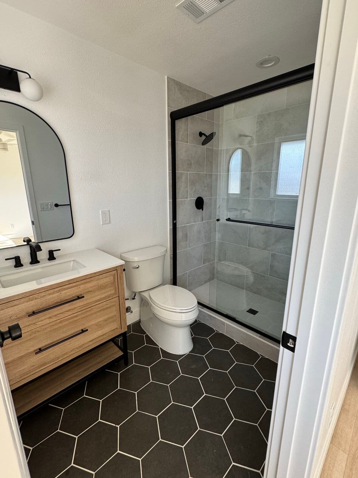 Walk-in shower in large-format gray tile with a black hexagon tile floor