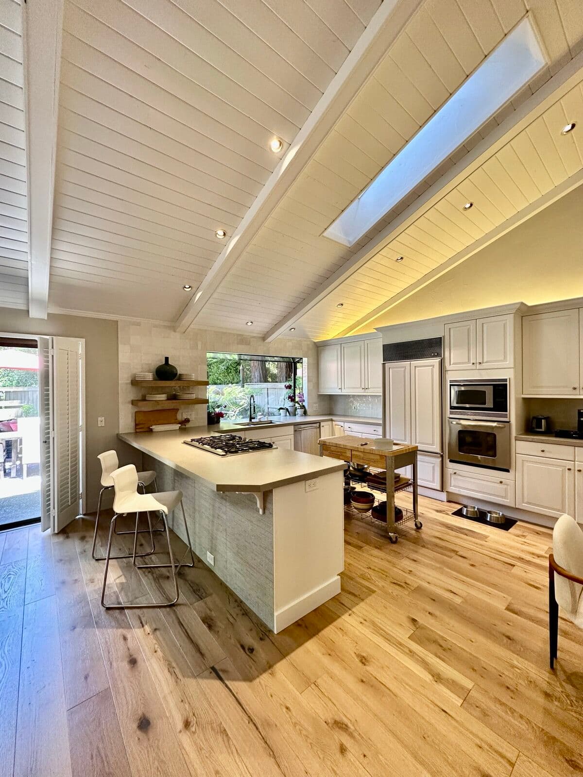 Finished kitchen layout with white cabinets and oak floor under a vaulted plank ceiling