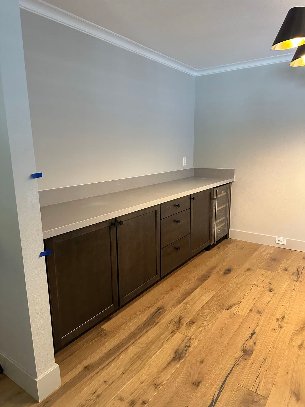 After — Wine-bar wall mid-install — stained base cabinets and wine fridge set but still without tops — versus the finished run with its quartz counter and backsplash, shot from the same spot.