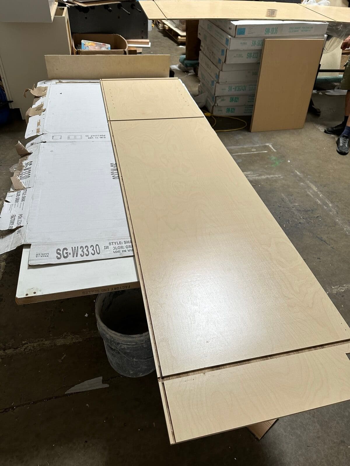 Birch plywood cabinet panels and labeled flat-pack boxes on a warehouse work table